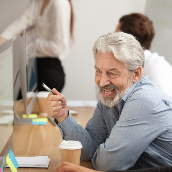 White-haired older businessman smiling and looking at a computer screen.