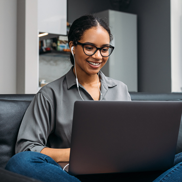 Young business woman wearing earbuds plugged into her laptop and looking at her screen.